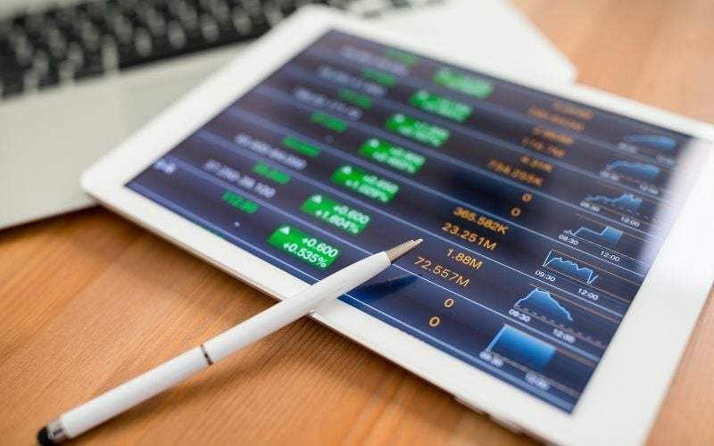 Image of a tablet that shows stock market rates and a pen beside a laptop