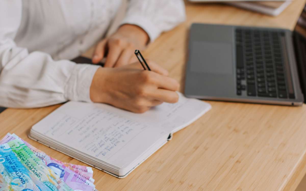 woman writing on her notebook with money beside_Awesome Benefits of Budgeting Your Money