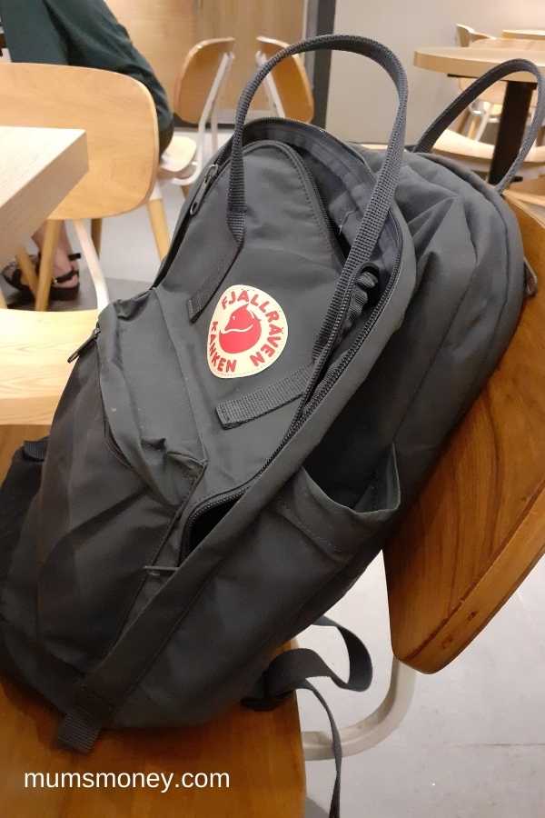 Grey backpack with red and white label placed on wooden chair