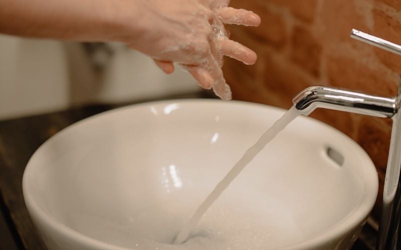a pair of hands with lather over a white sink with running water from the faucet