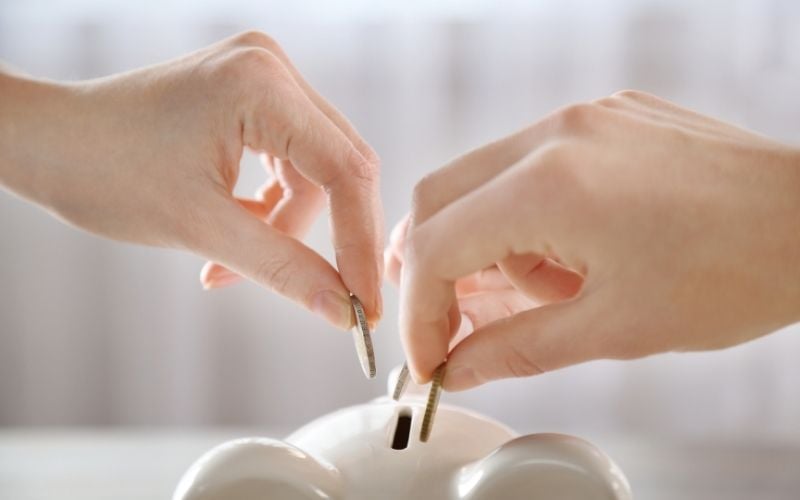 Photo of two hands holding coins over a piggy bank
