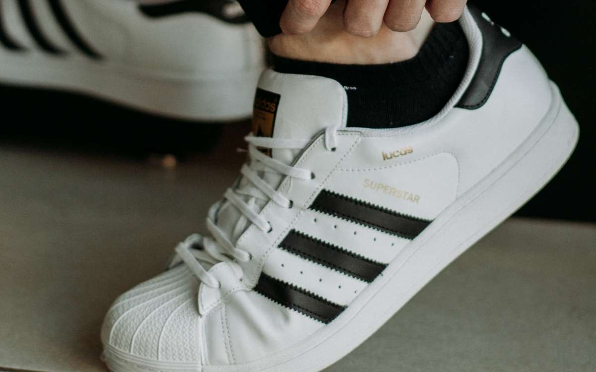 a foot wearing a white Adidas shoe with a hand on the leg