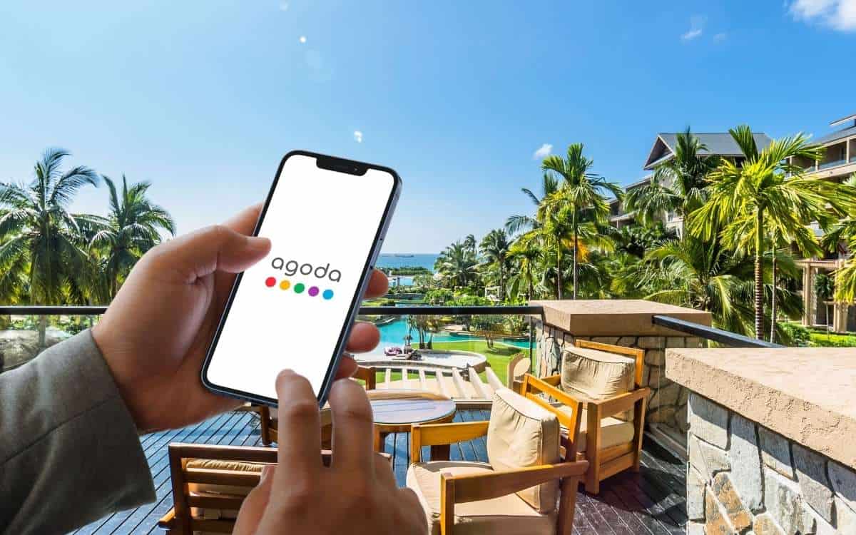 A pair of hand holding a cellphone with Agoda logo on it with resort background