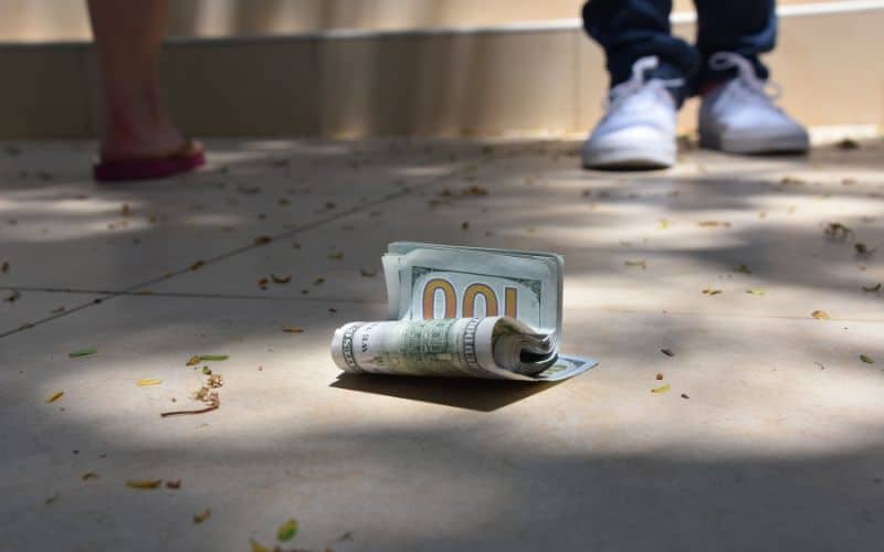 Photo of a pair of feet in white shoes coming towards the money on the ground.