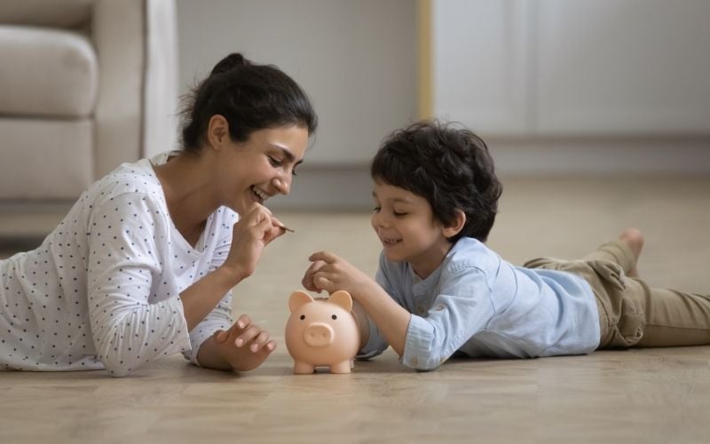 Photo of a happy woman and a boy holding coin over a piggy bank