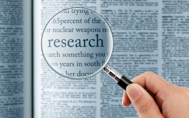 Photo showing a magnifying glass held by a hand that focus on the word Research