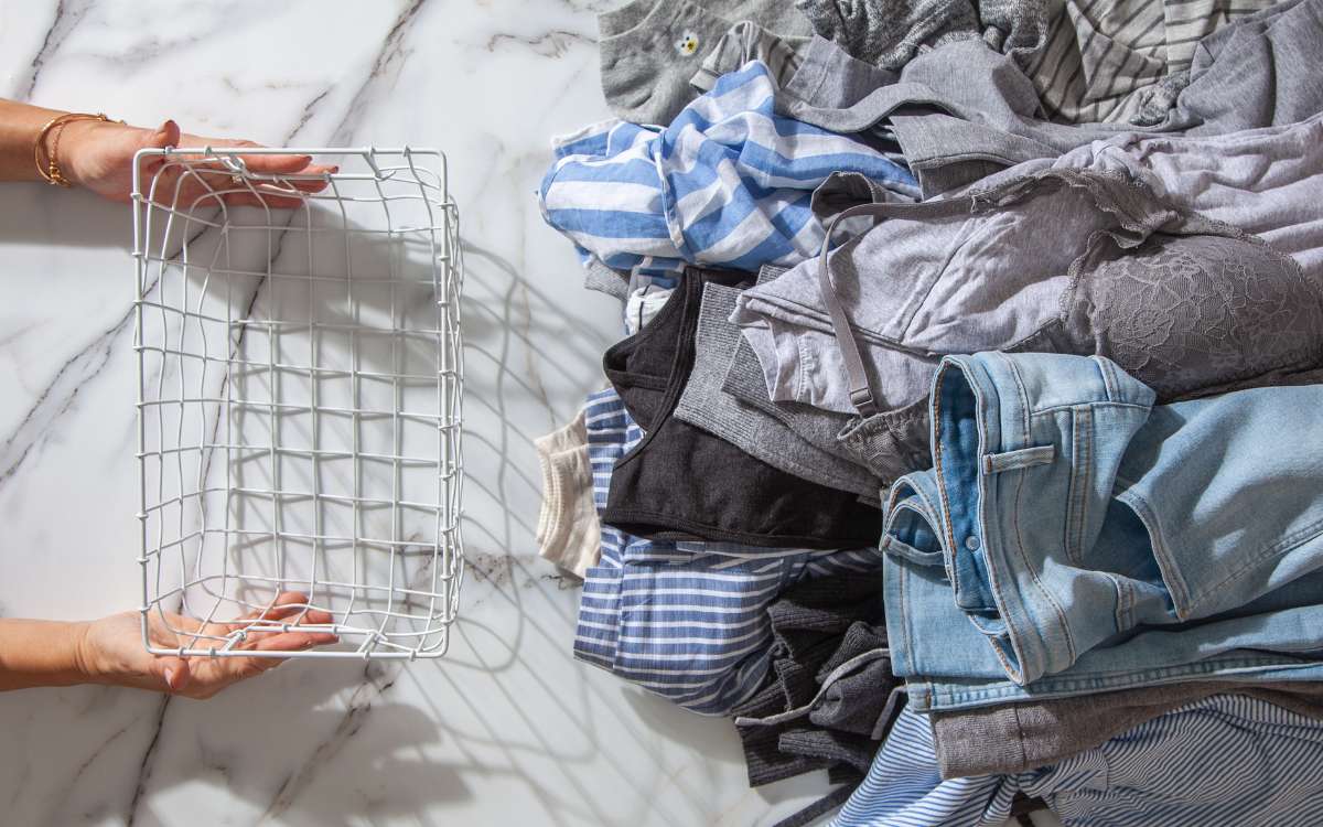 Simple Decluttering Tip_pair of hands holding a basket placed near cluttered clothes.