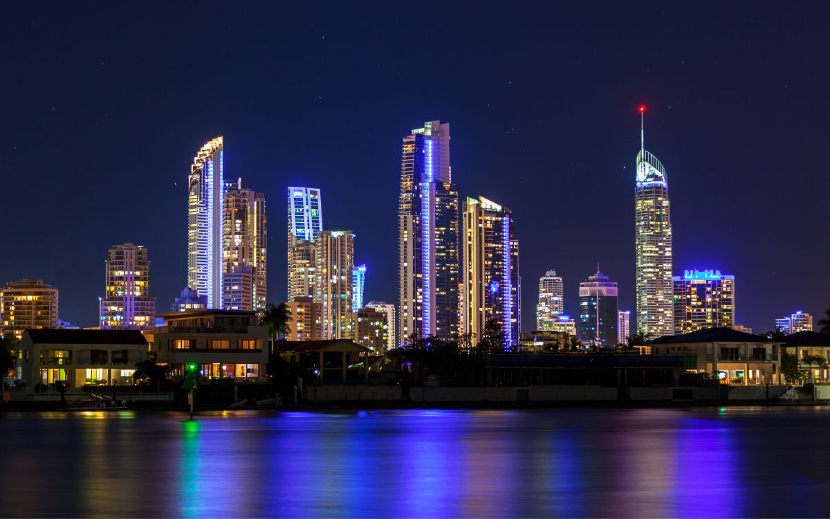 Gold Coast skyline at night with illuminated high-rise buildings reflecting on the water.