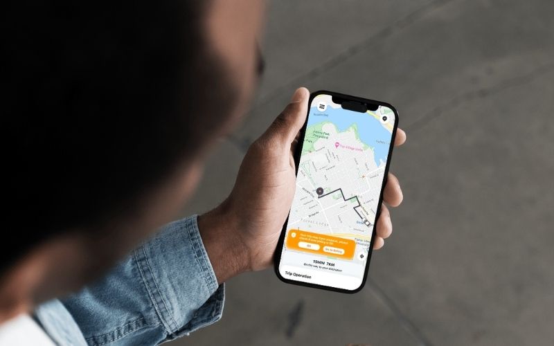 An over-the-shoulder shot of a person holding a smartphone that displays a navigation map with a routed path.
